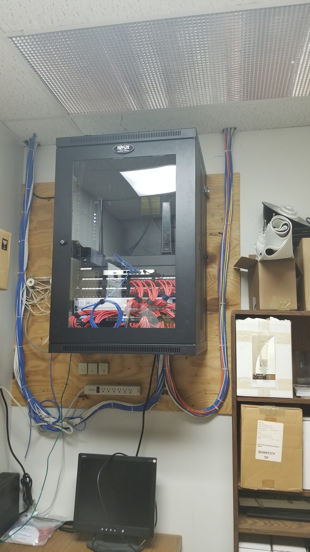 Glass-front network cabinet installed on a commercial backboard with service cabling dressed around it