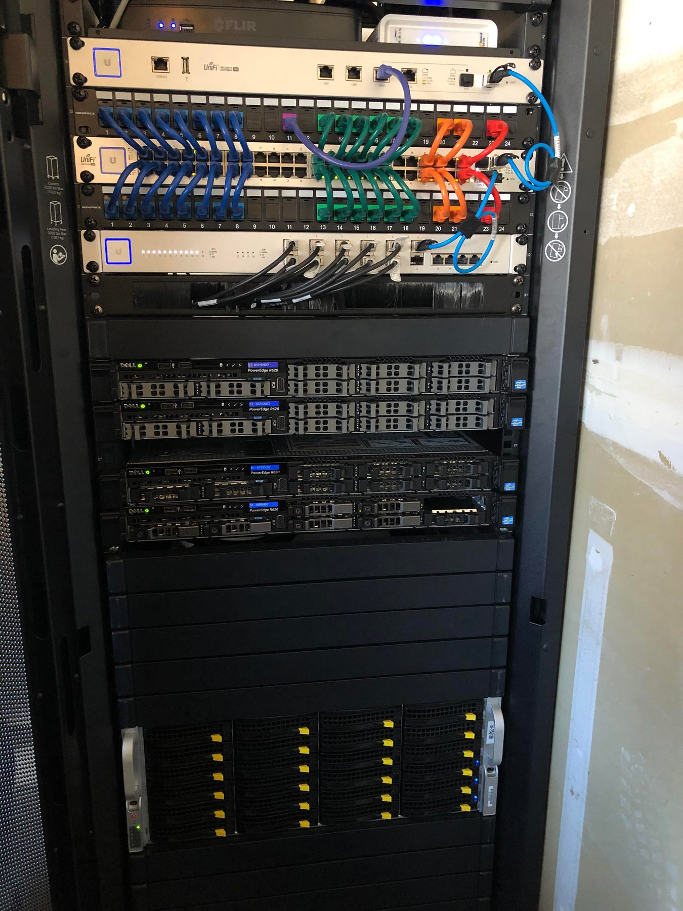 Full-height commercial rack with color-coded network switching, rack servers, and storage arrays
