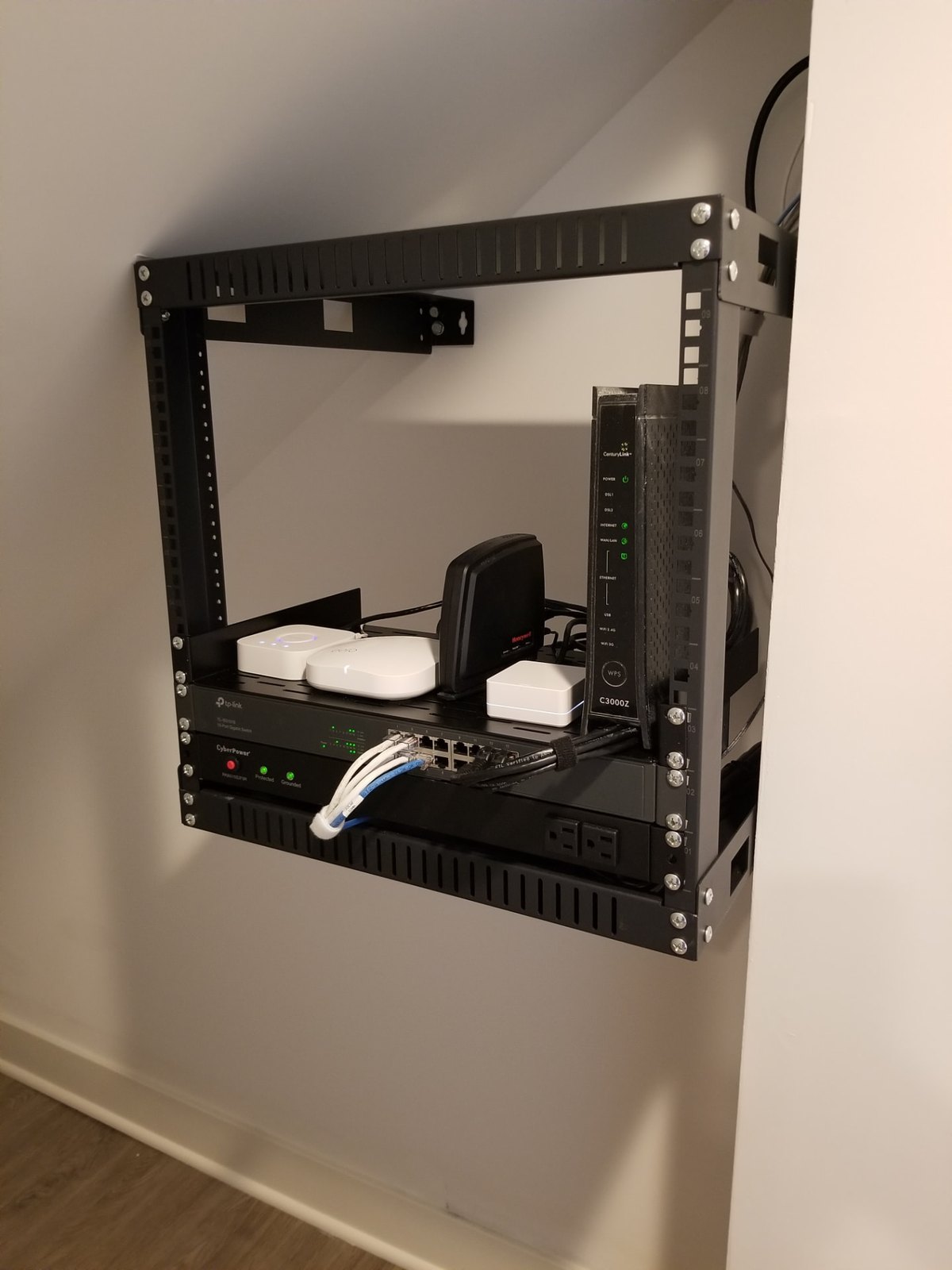 Wall-mounted residential network rack installed beneath a staircase with network and power equipment organized on shelves