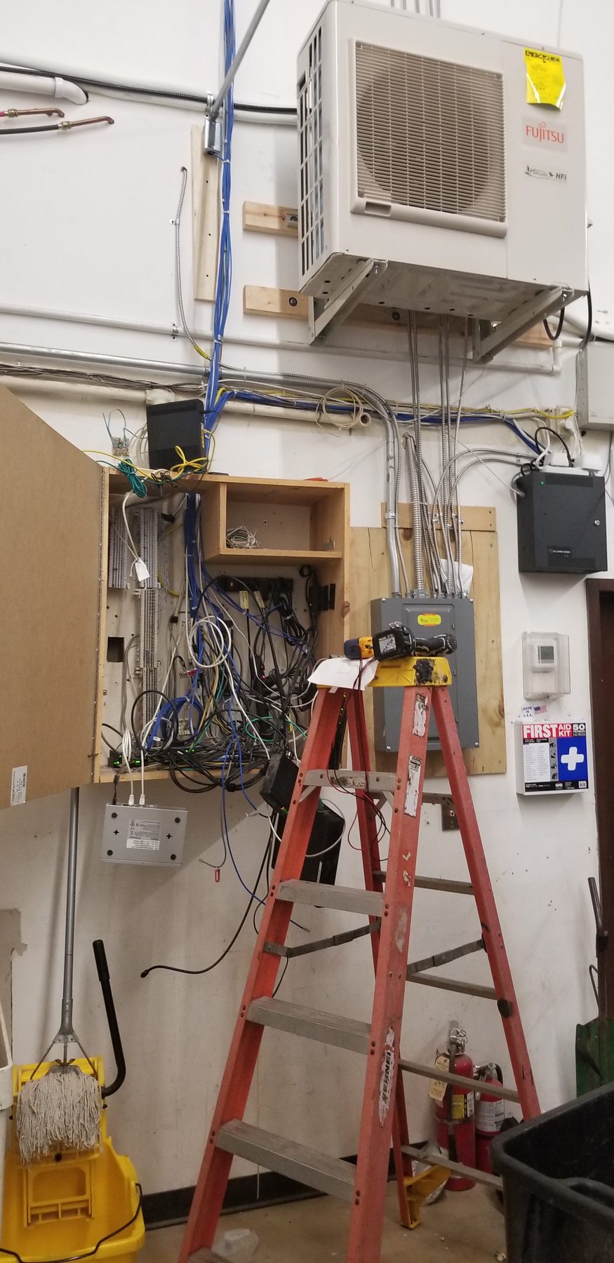 Industrial utility wall before cleanup with loose network equipment and cabling in an open wooden enclosure