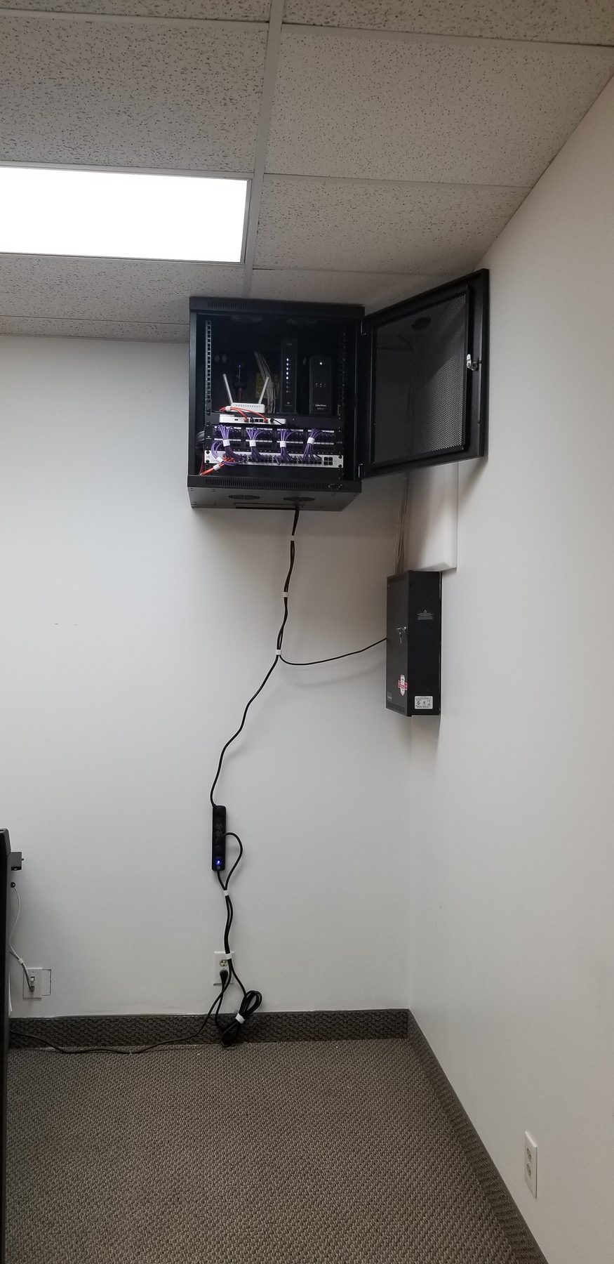 Wide view of a compact wall-mounted network cabinet installed high in an office
