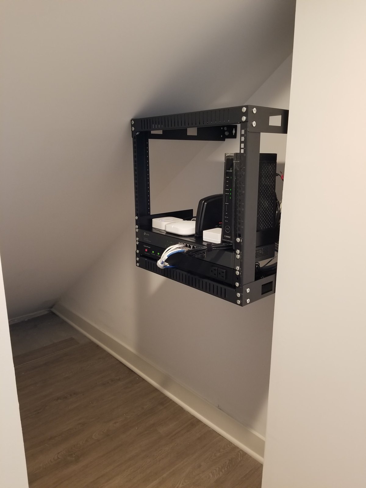 Wide view of a compact residential network rack mounted in the finished space under a staircase