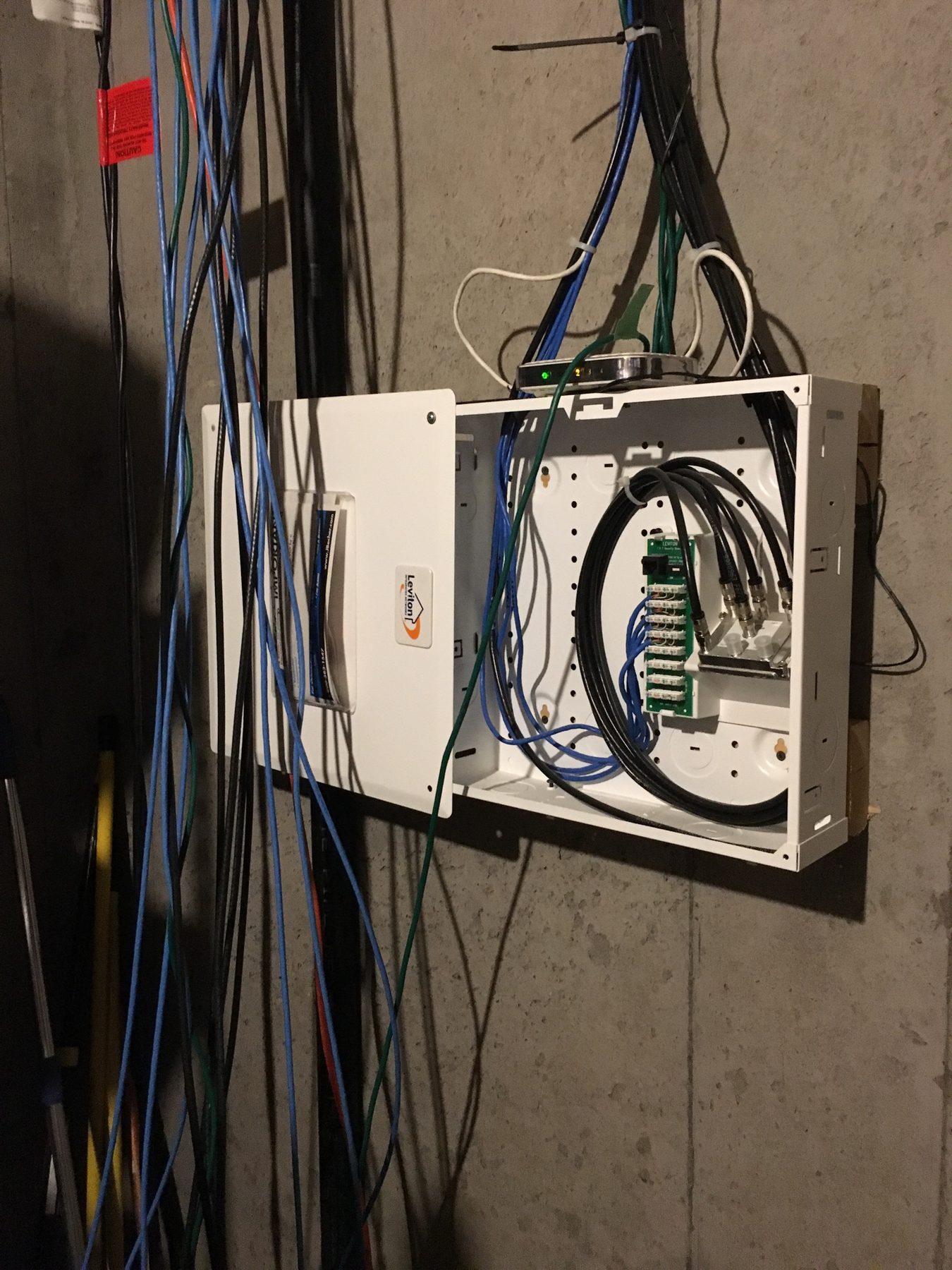 Before cleanup showing loose category and coax cabling around a residential media panel on a concrete basement wall
