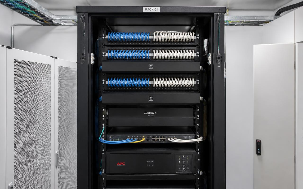 After: a professionally organized commercial network rack with labeled patch panels, dressed patch cables, fiber enclosure, and rack-mounted UPS