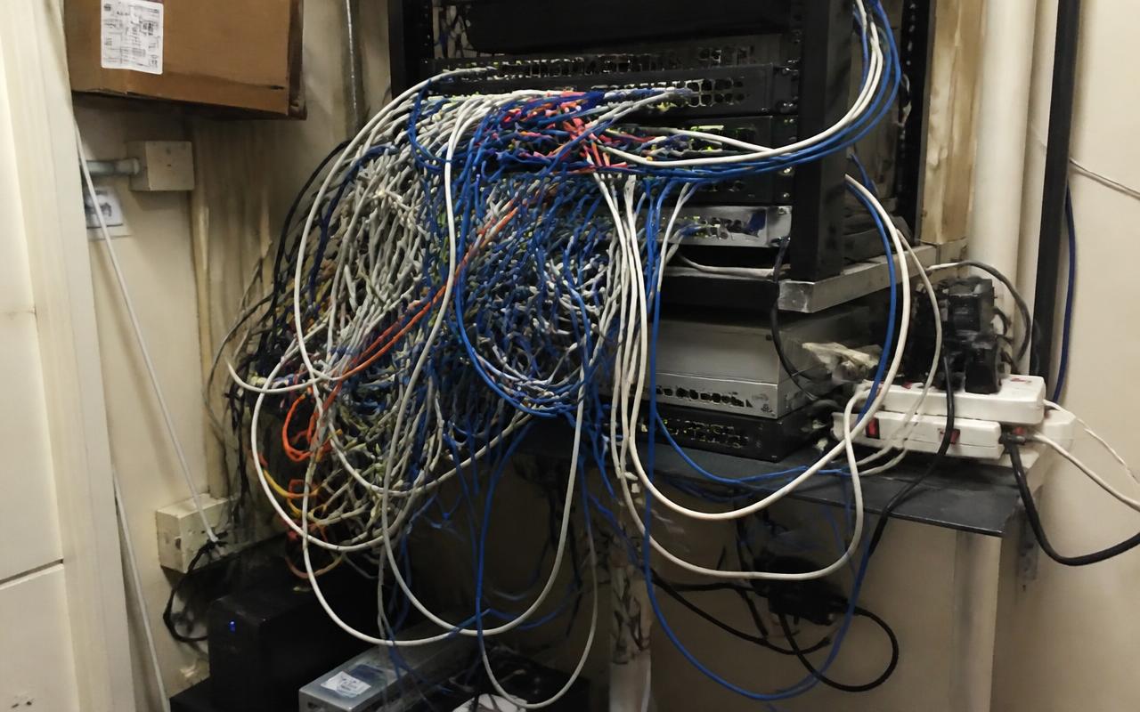 Before: a messy commercial network closet with tangled unlabeled cables, stacked switches, and daisy-chained power strips