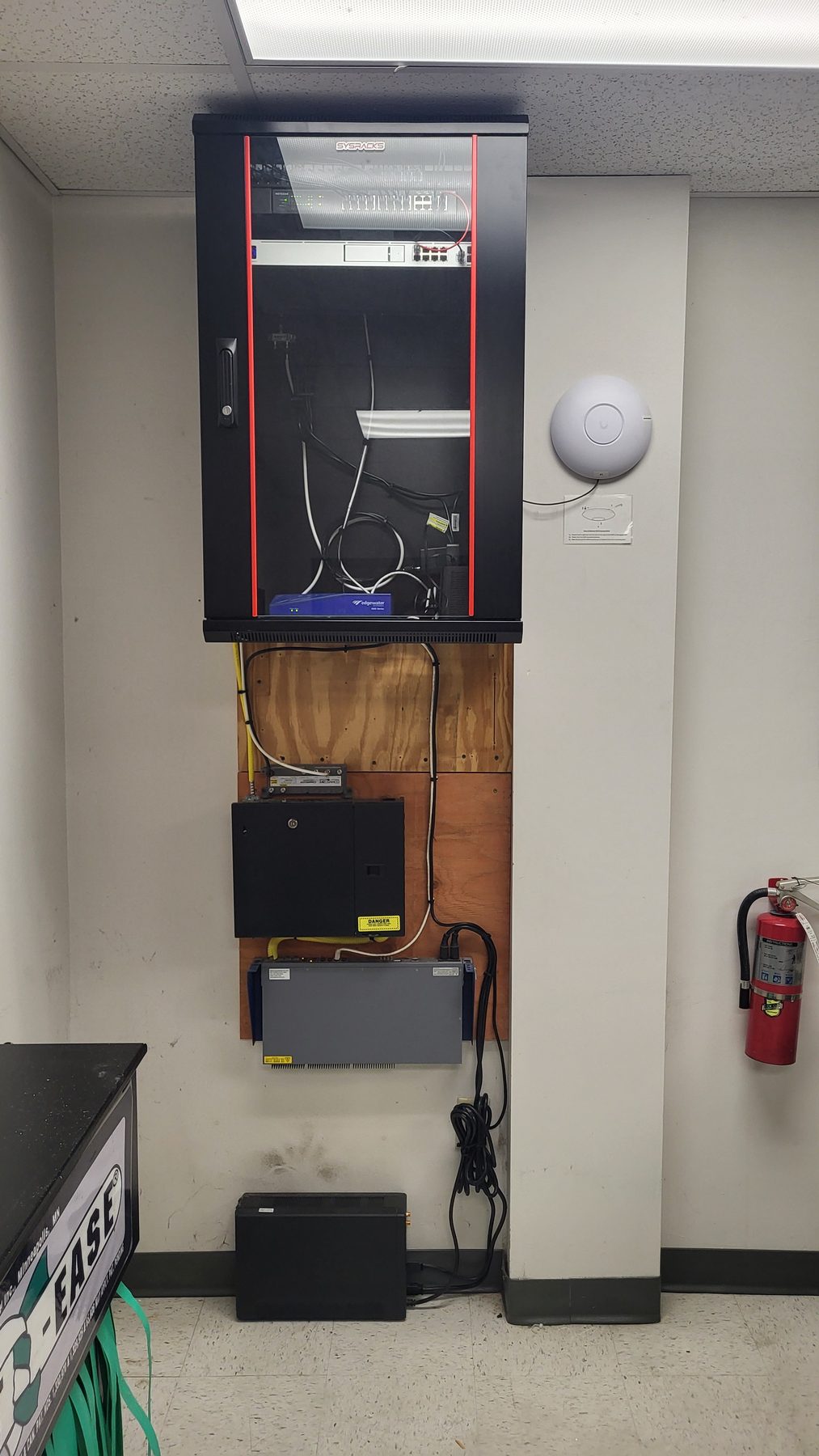 Closed wall-mount network cabinet installed above the backboard with cabling routed neatly behind it