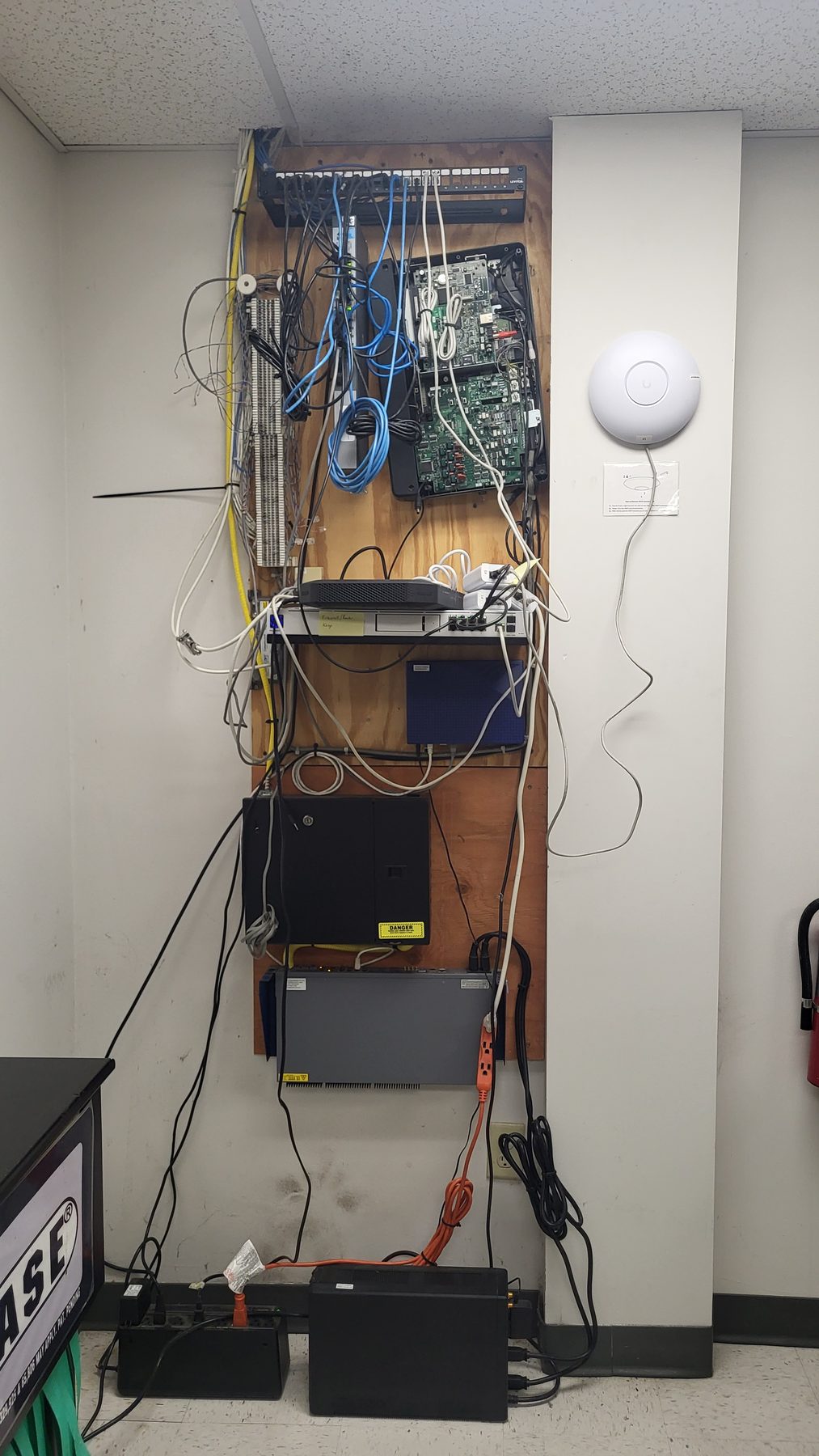Network equipment and loose blue and white cabling mounted directly to a plywood backboard before the upgrade
