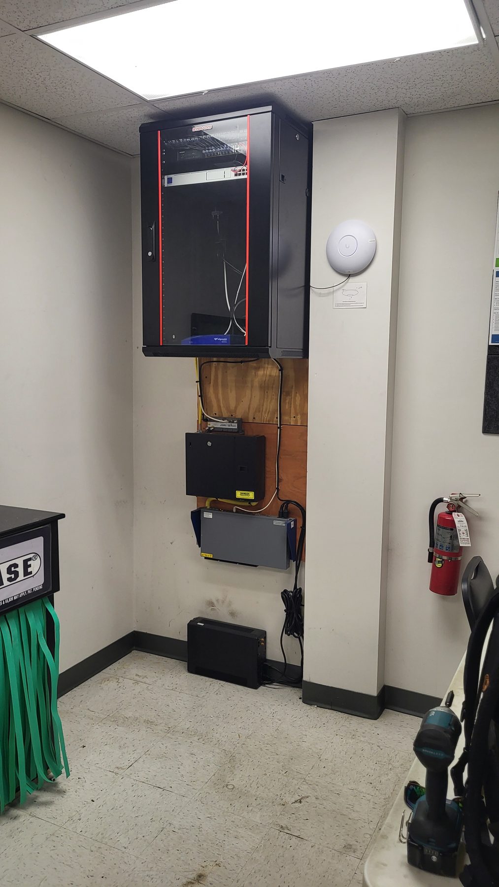 Angled view of the finished network cabinet, backboard, and battery backup along the office wall