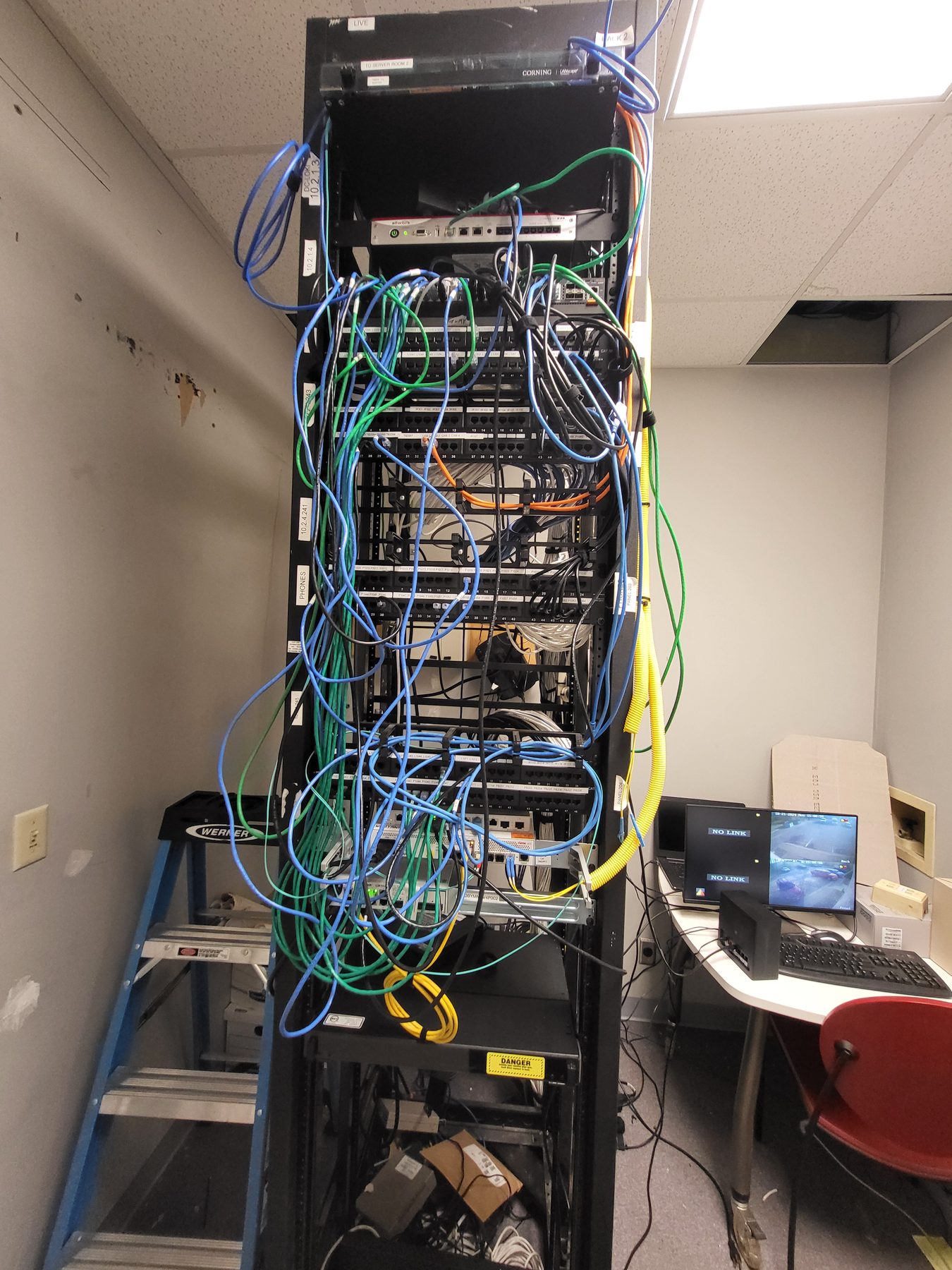Floor-standing network rack with long loops of colored patch cords hanging loosely across the front before cleanup