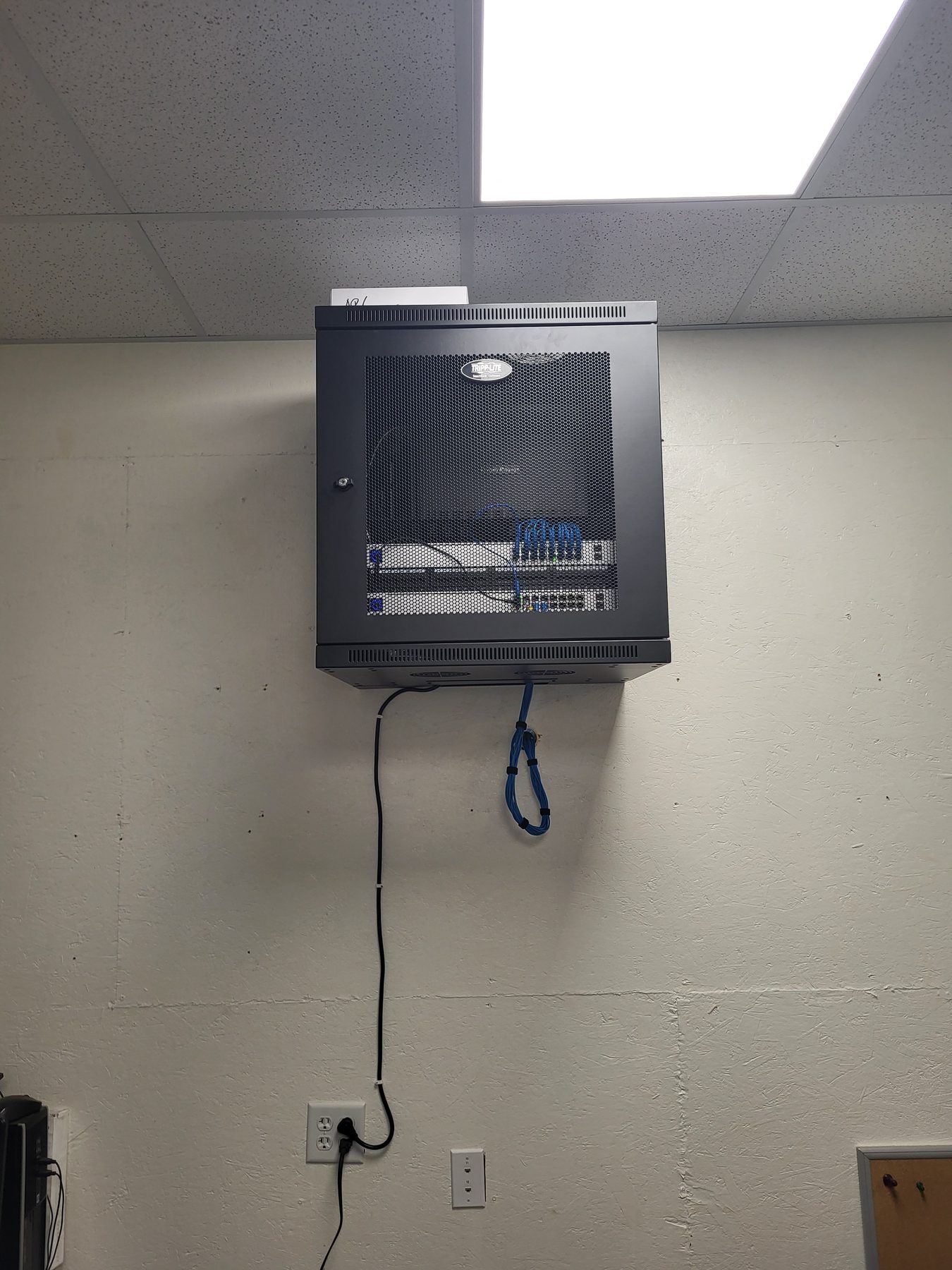 Closed wall-mount network cabinet with a single service cable dropping down the wall to an outlet