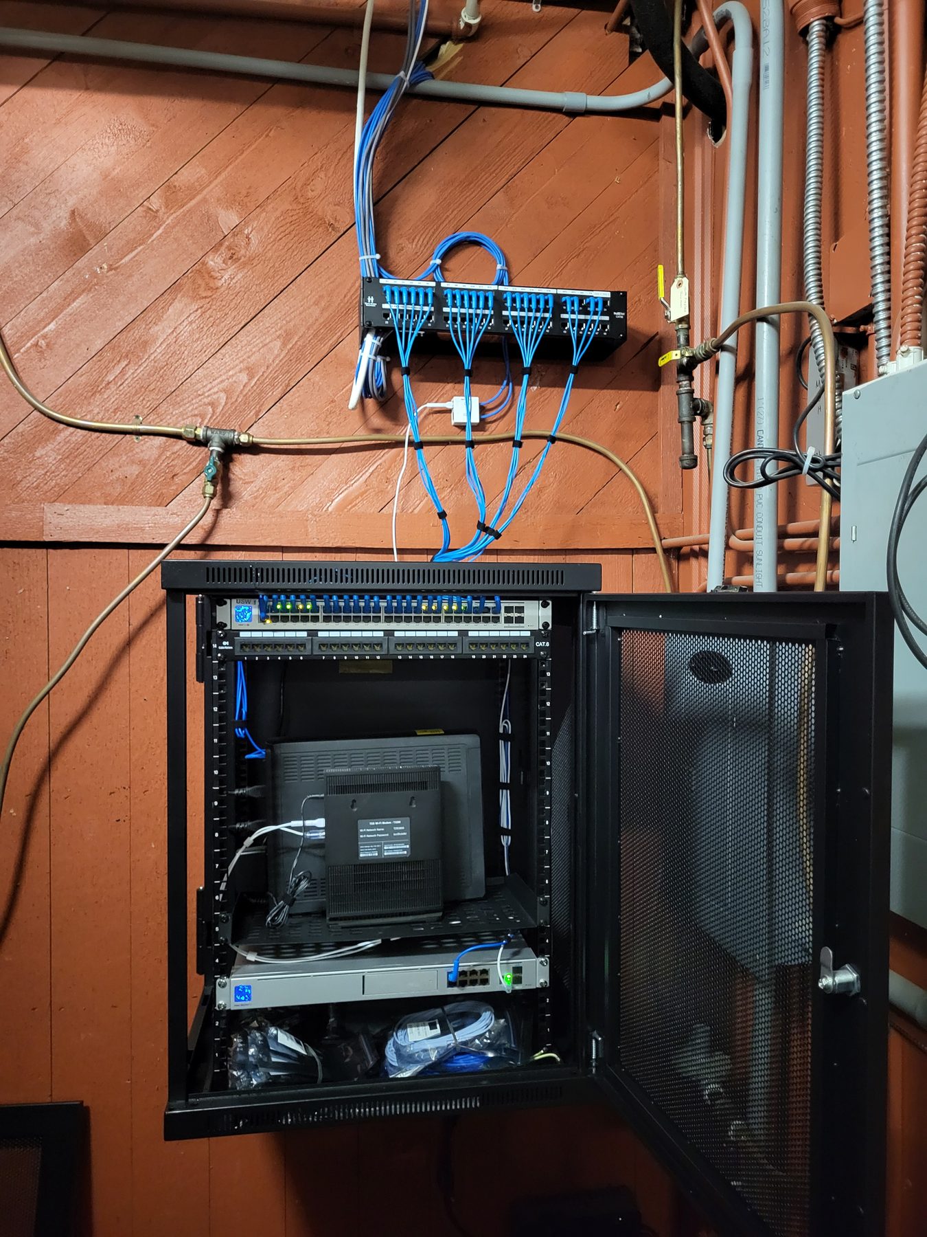 Patch panel above an open network cabinet in a mechanical area, with cabling dressed along the wall