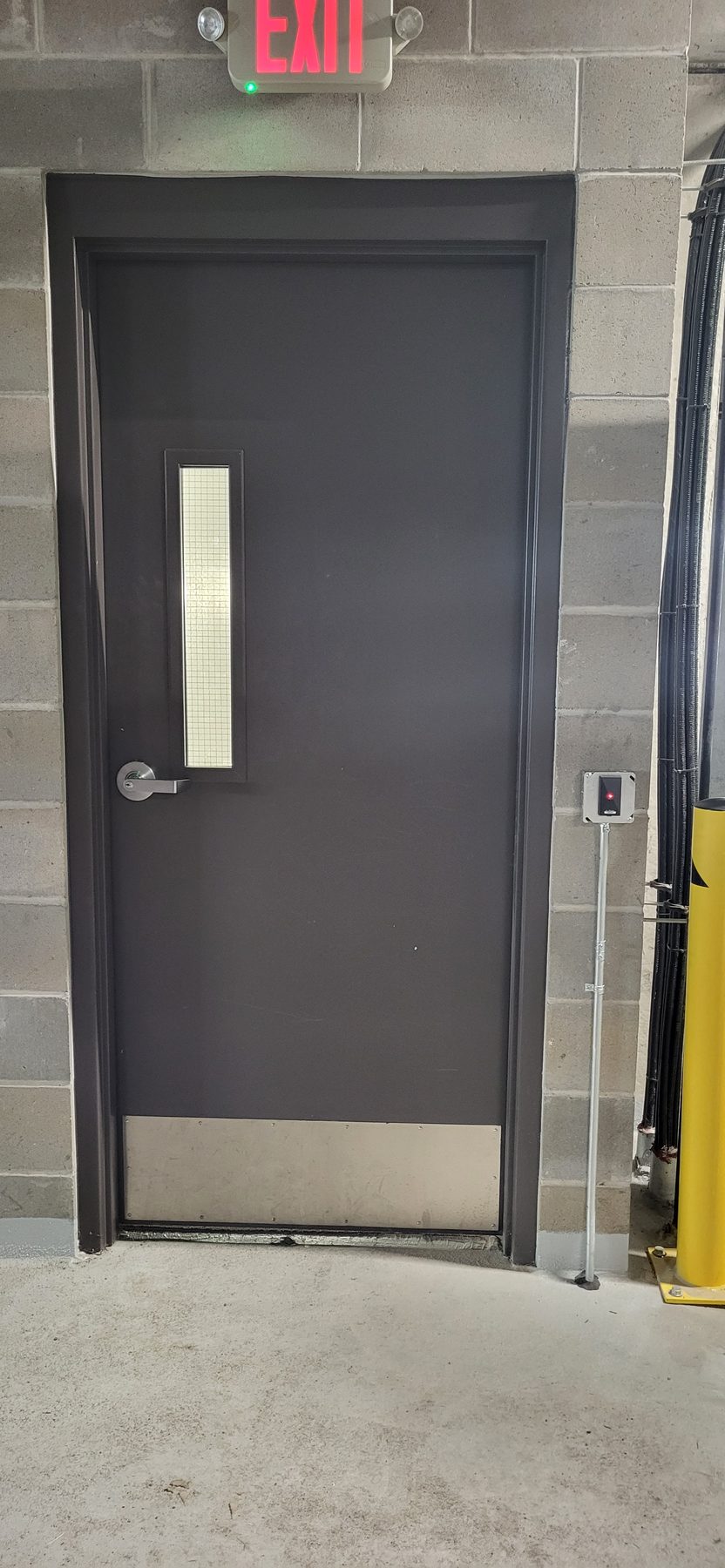 Grey steel door with a card reader on a stand-off mount and exposed conduit feeding the opening