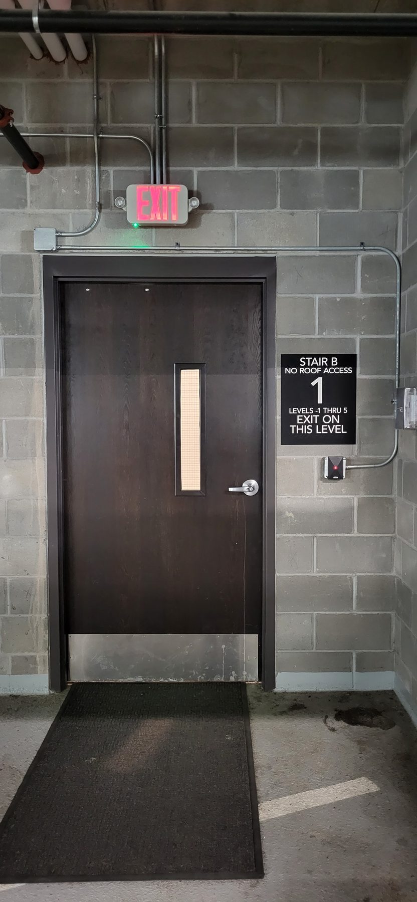 Interior stairwell door with a card reader beside it and conduit running up the block wall to the ceiling
