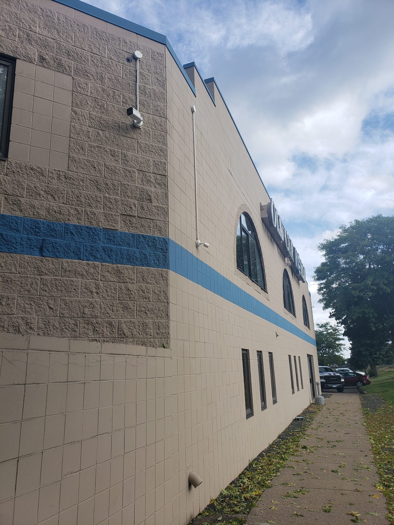 Building side wall with a camera on a stand-off arm angled down toward the parking area