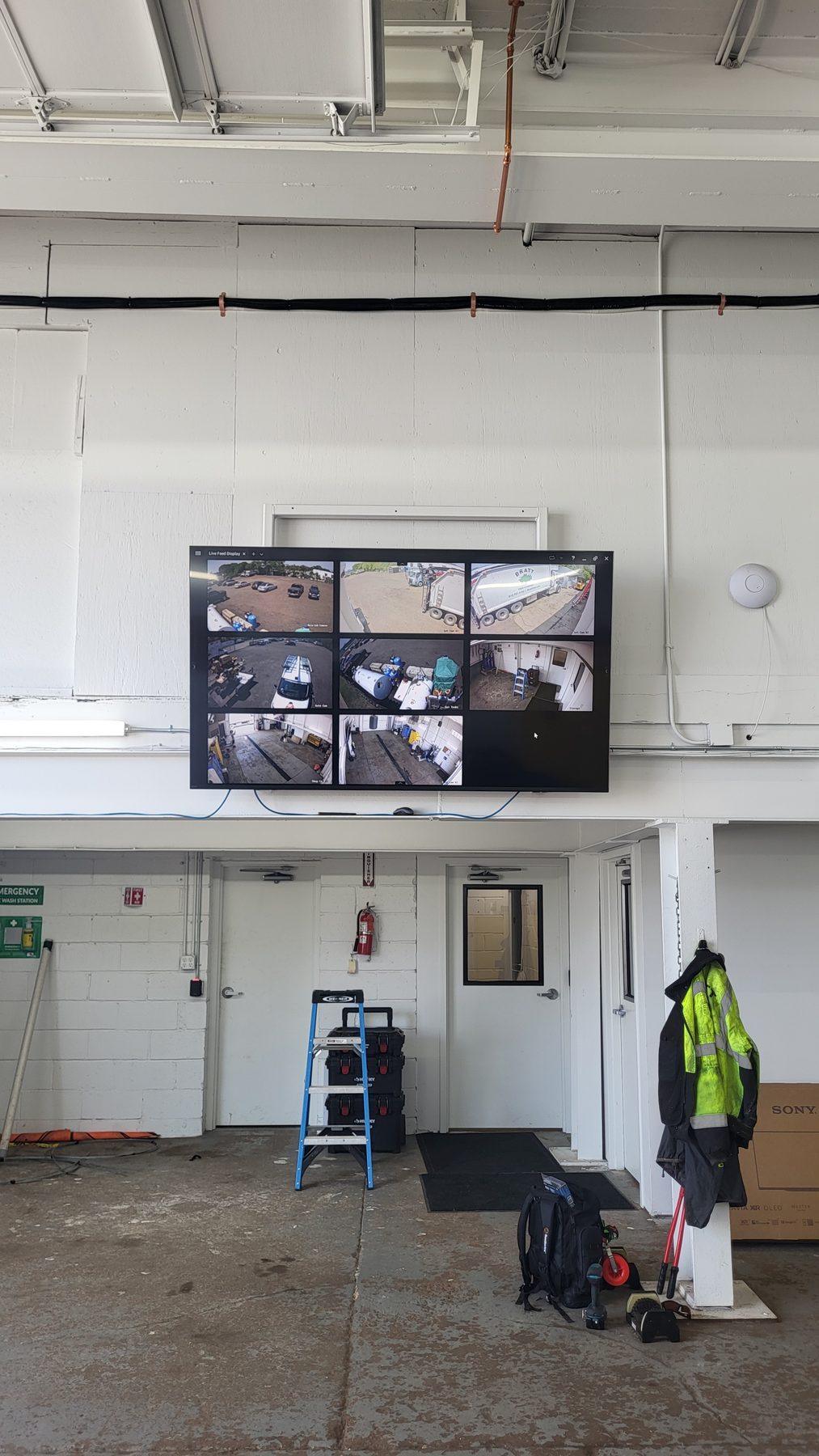 Wall-mounted display in a shop showing a multi-camera grid of the yard and interior work areas